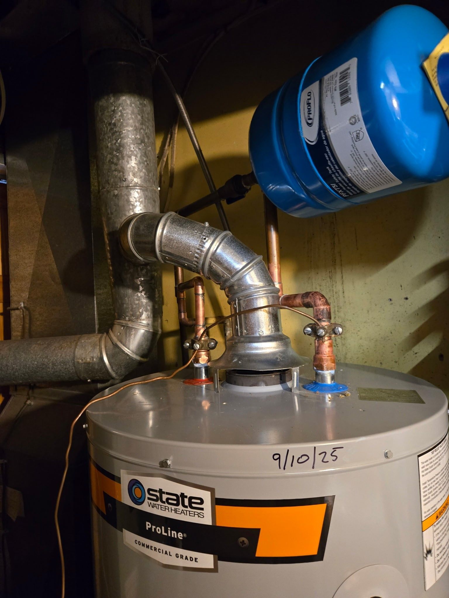 A State brand water heater with a blue expansion tank and silver exhaust vent pipe installed in a utility space.