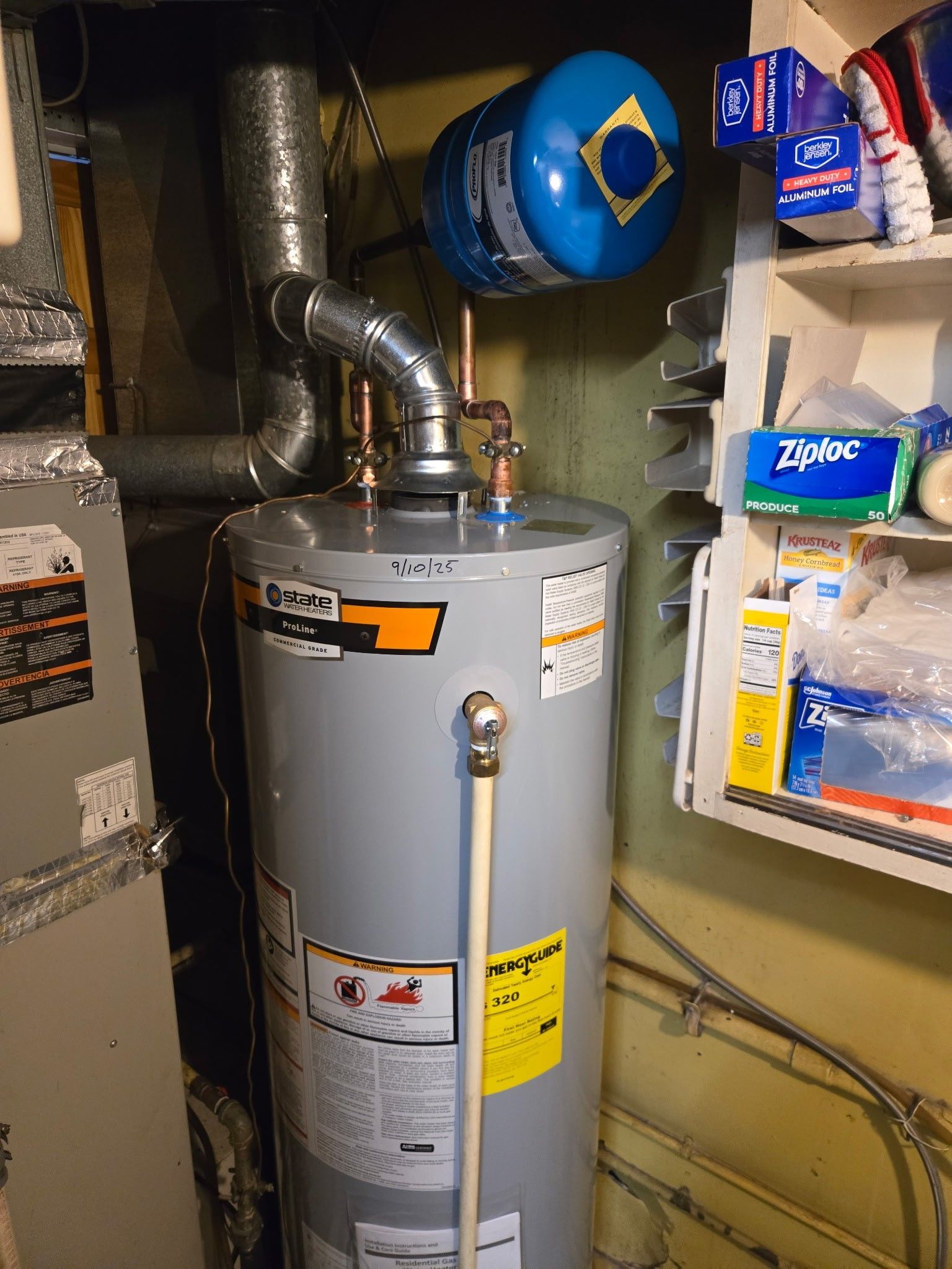 A gray water heater with a blue expansion tank on top, positioned in a utility area next to shelving.