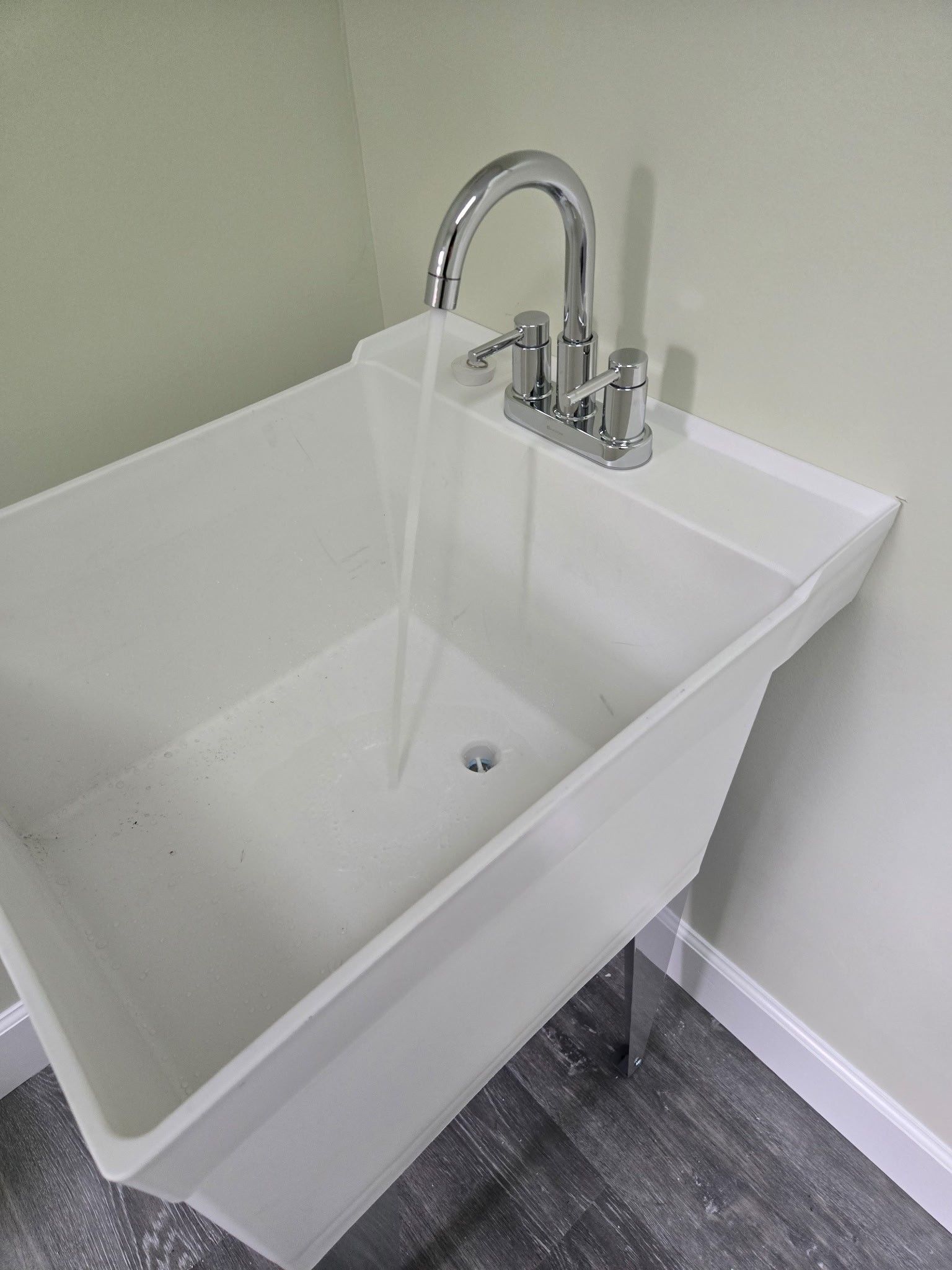 A white utility sink with a chrome faucet running water, positioned against a light-colored wall.