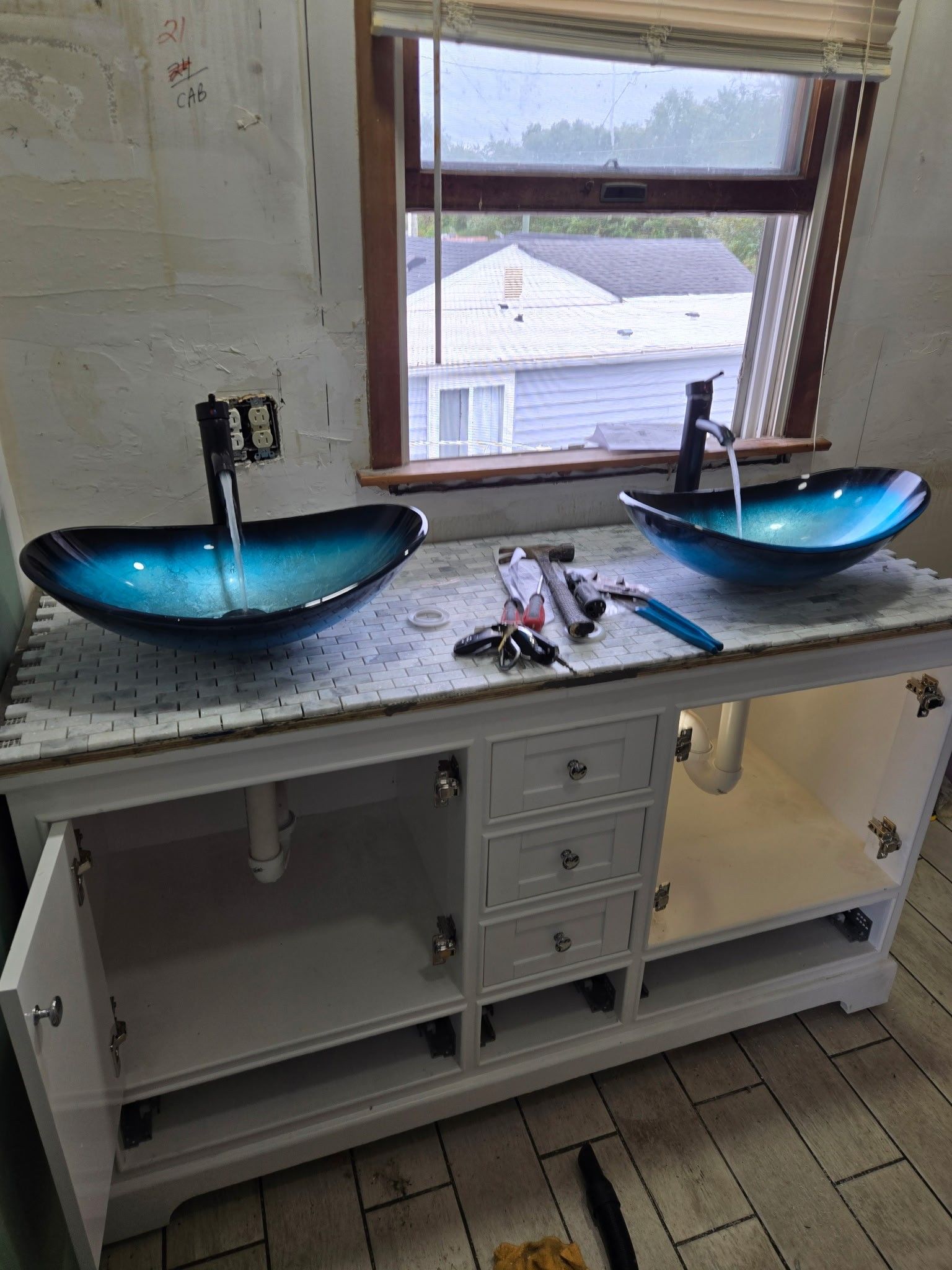A double vanity with blue glass vessel sinks and faucets installed on a white countertop, inside a room under construction.