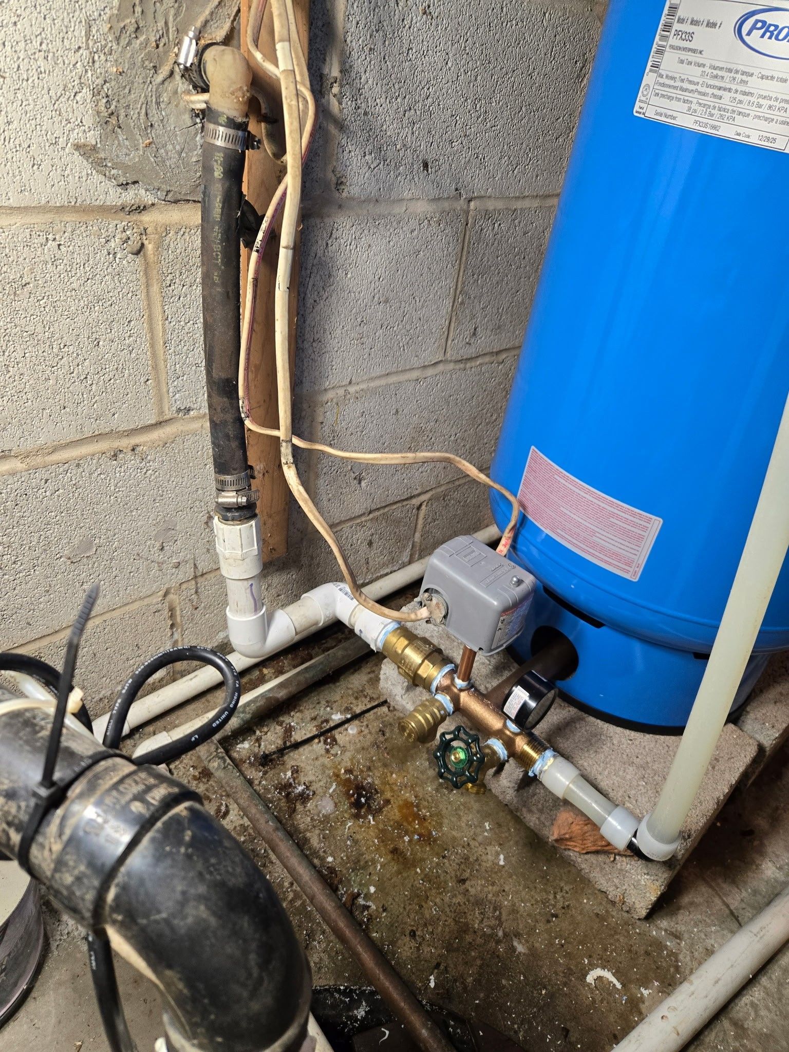 A blue well pressure tank with plumbing connections, a pressure switch, and a small puddle of water on a concrete floor.