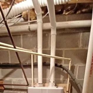 Basement with pipes, furnace, and exposed brick. Some pipes are white PVC, others are metal.