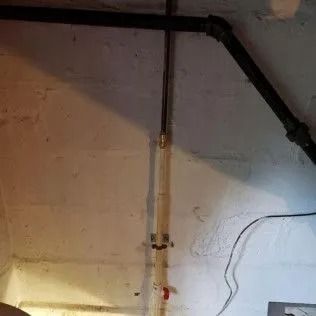 Pipes and wall in a basement. Black and white pipes on the wall, red valve at the bottom.