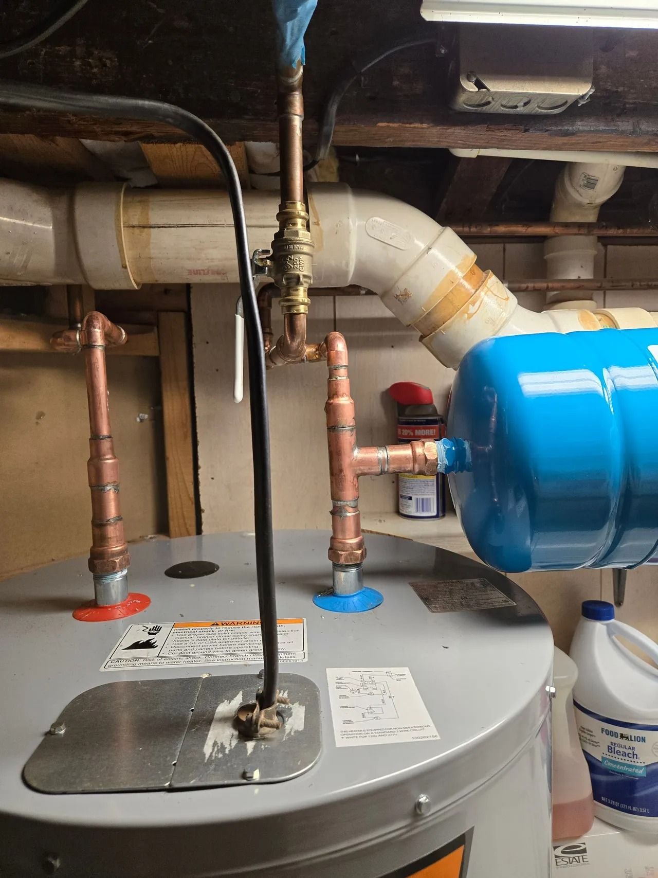 A water heater with copper pipes, a blue expansion tank, and a black electrical cable in a basement setting.