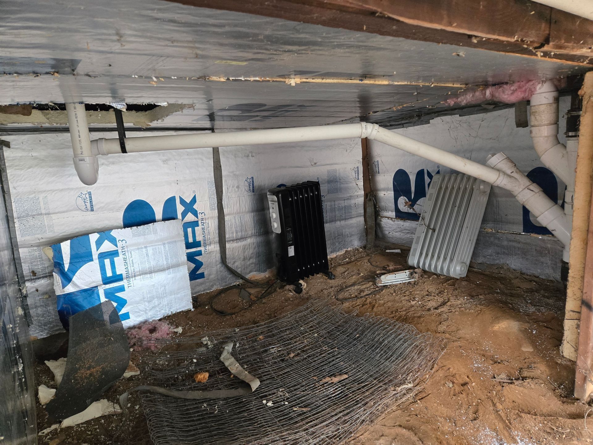 Crawlspace with insulation, pipes, and debris. Walls are partially insulated with foam.