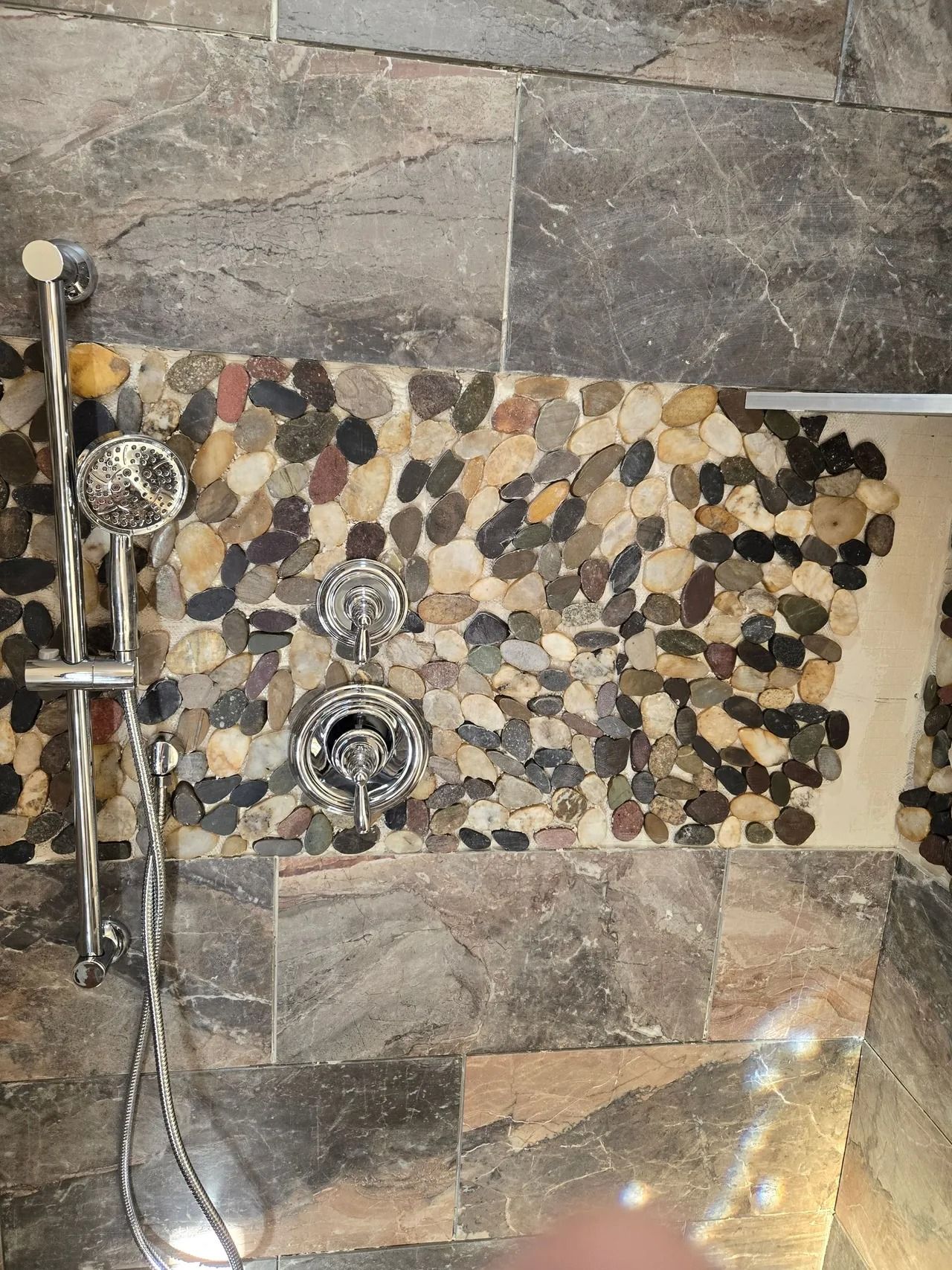 Shower with stone tile walls, a pebble tile accent, and chrome shower fixtures.