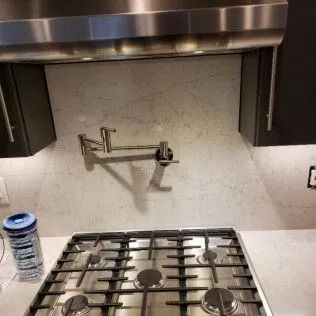 Kitchen with stovetop, pot filler, and light gray backsplash.
