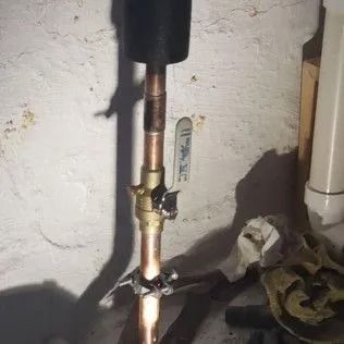 Copper pipes with a valve against a white wall in a basement.