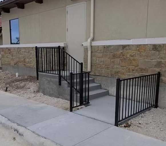 Black metal railing and steps leading to a door on a building with stone and tan siding.