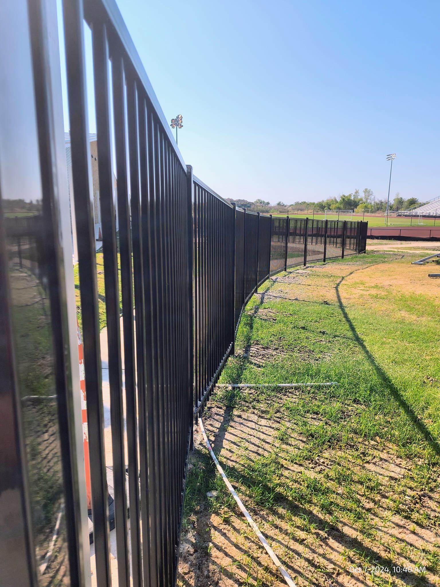 Black metal fence curving along a grassy area under a blue sky.