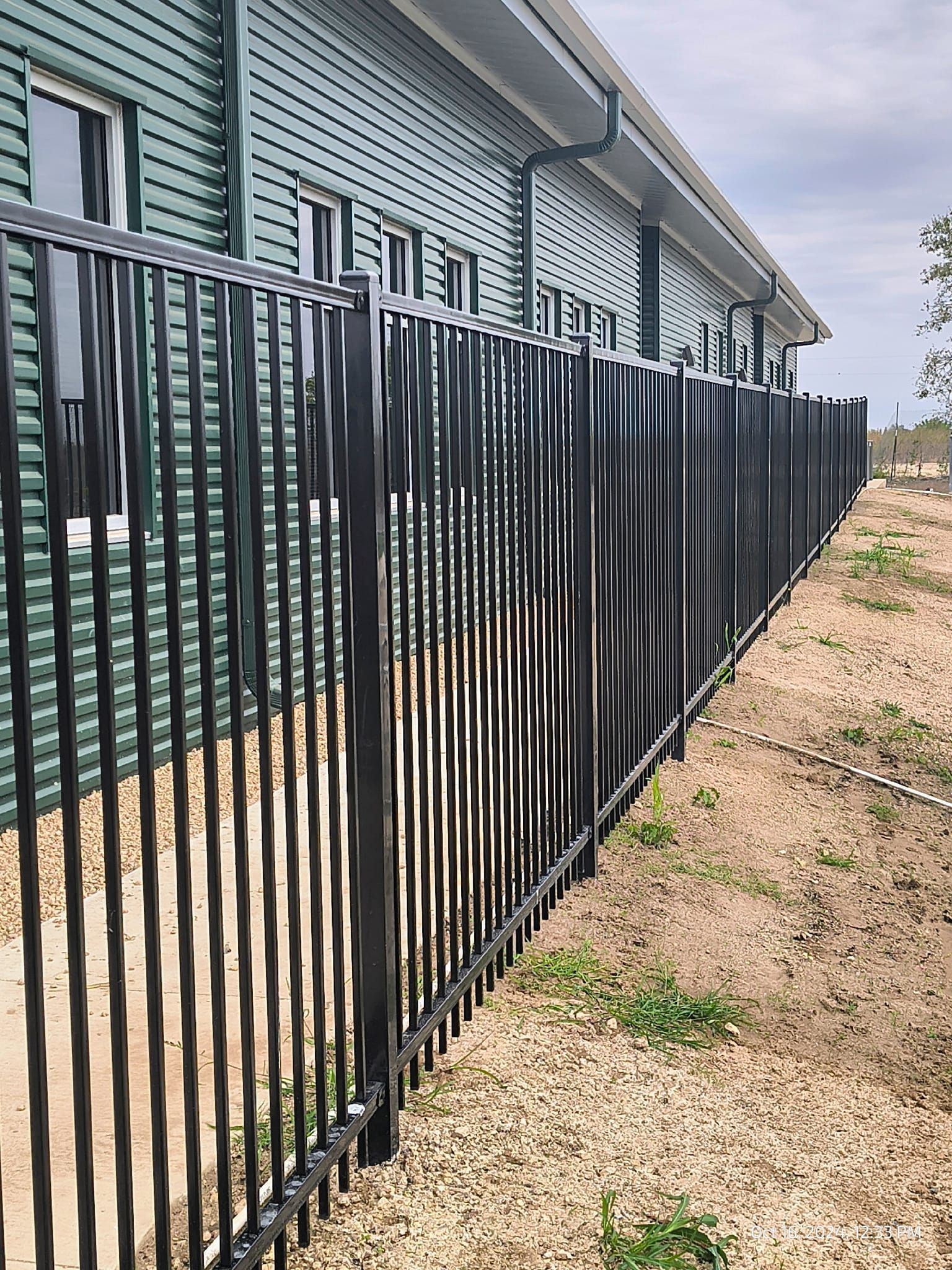Black metal fence bordering a grassy yard, with a brick building in the background.