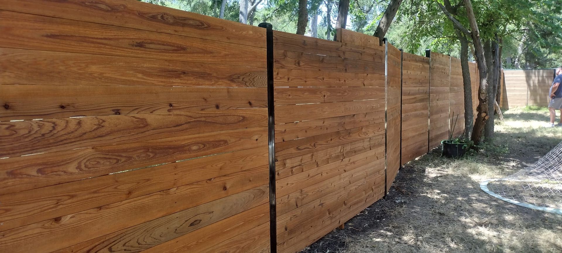 Wooden fence in a natural setting. Brown wood, curved shape, trees in the background, blue sky.