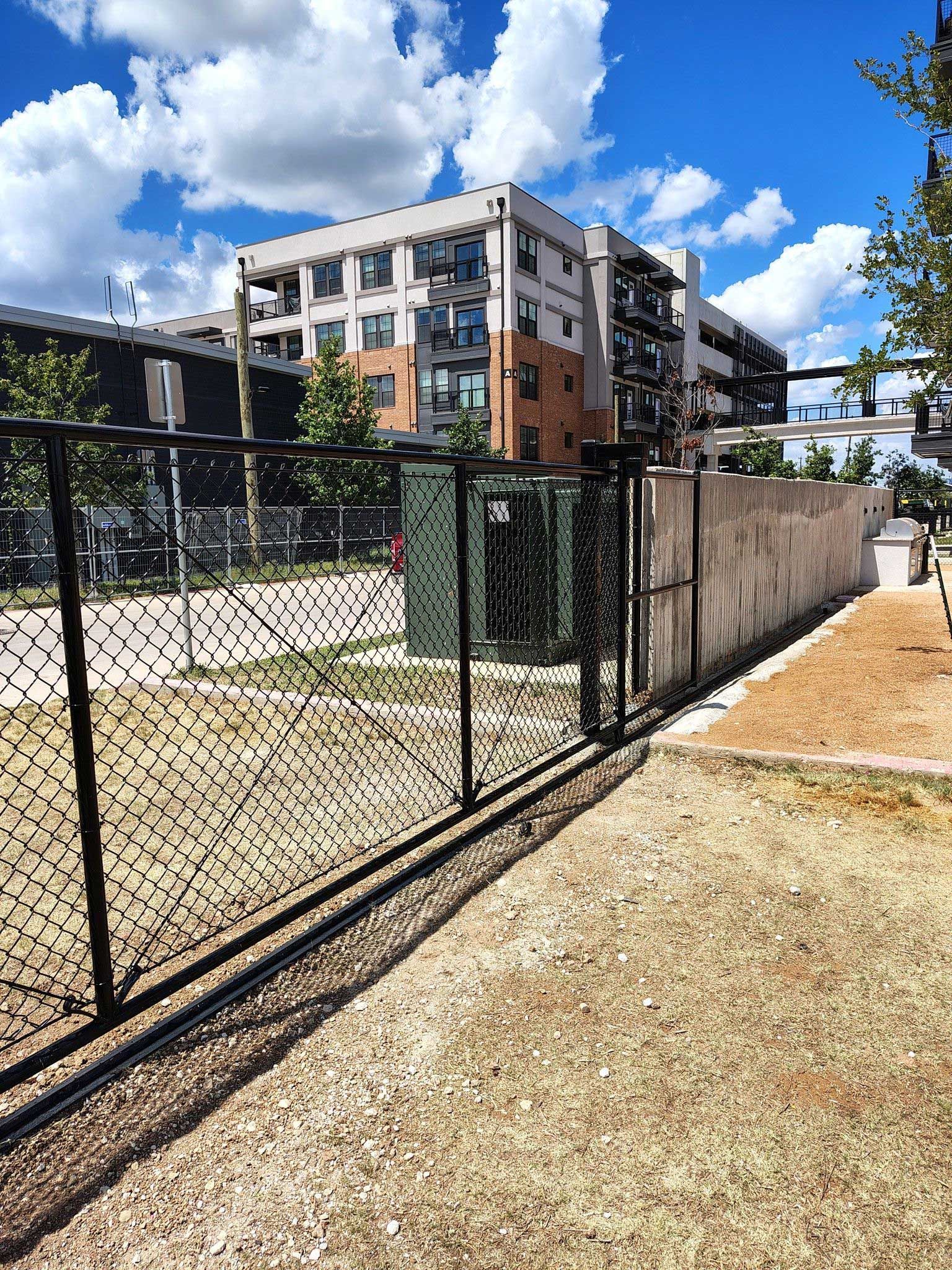 Black fence in front of a building with a cloudy sky. Brown grass in the foreground.