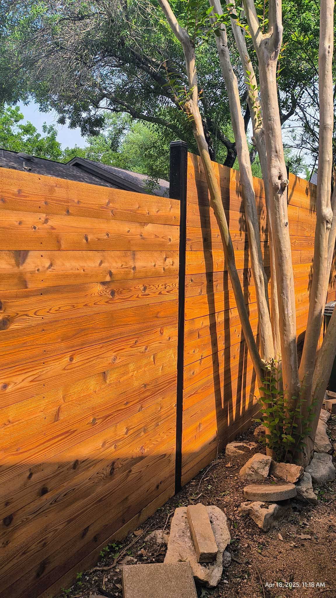 Wooden fence with natural wood grain, dark posts, and trees casting shadows.