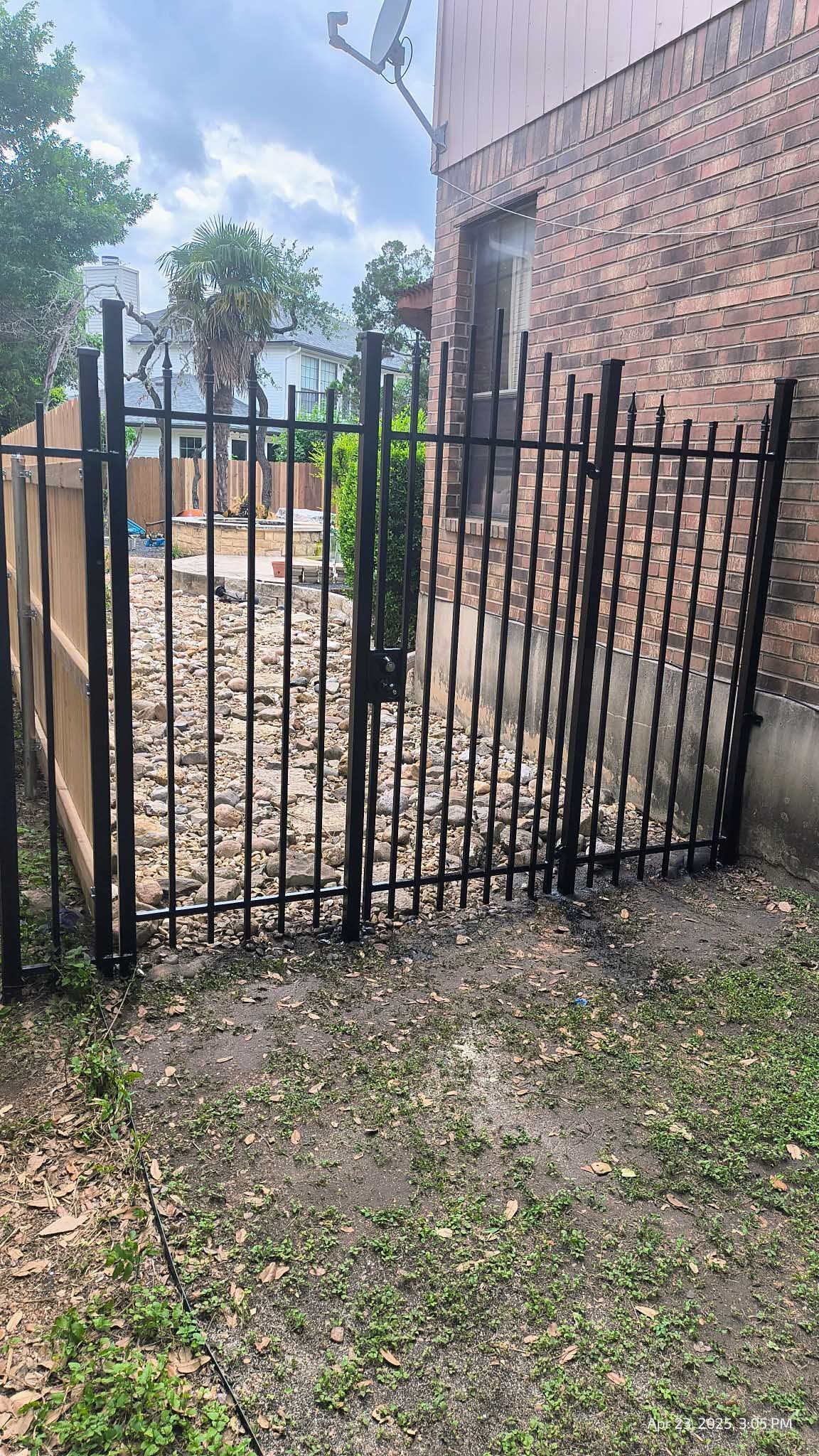 Black metal fence gates open onto a dirt area near a brick building.