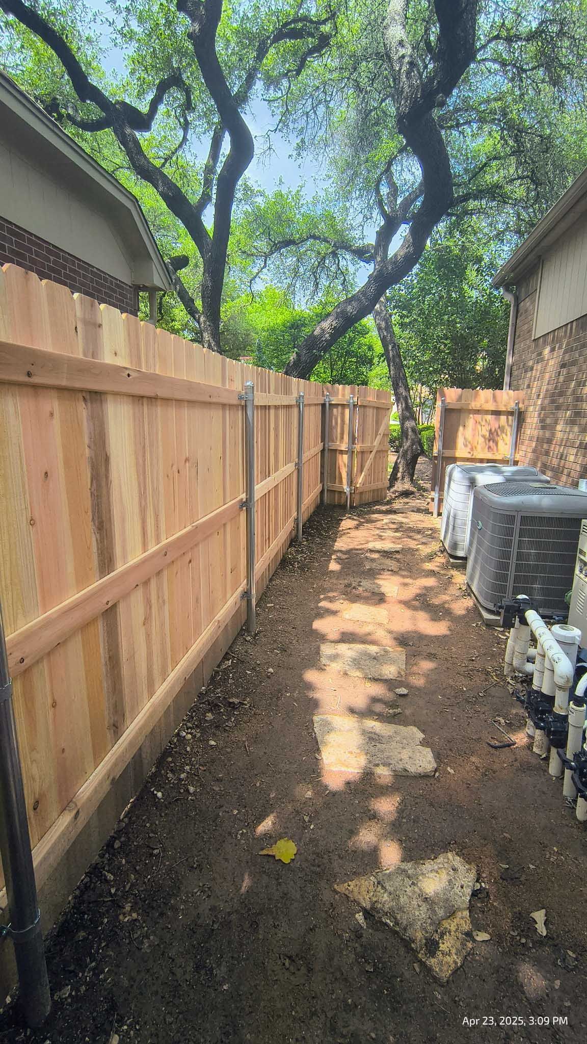Wooden fence alongside a narrow, dirt pathway with trees in the background.