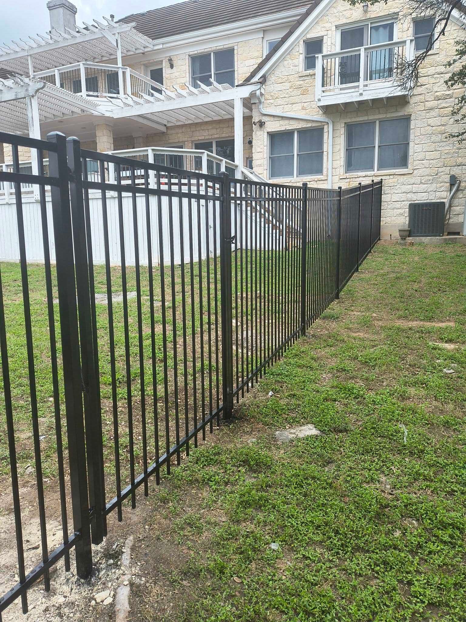 Black metal fence along a grassy yard, beside a light-colored brick house.