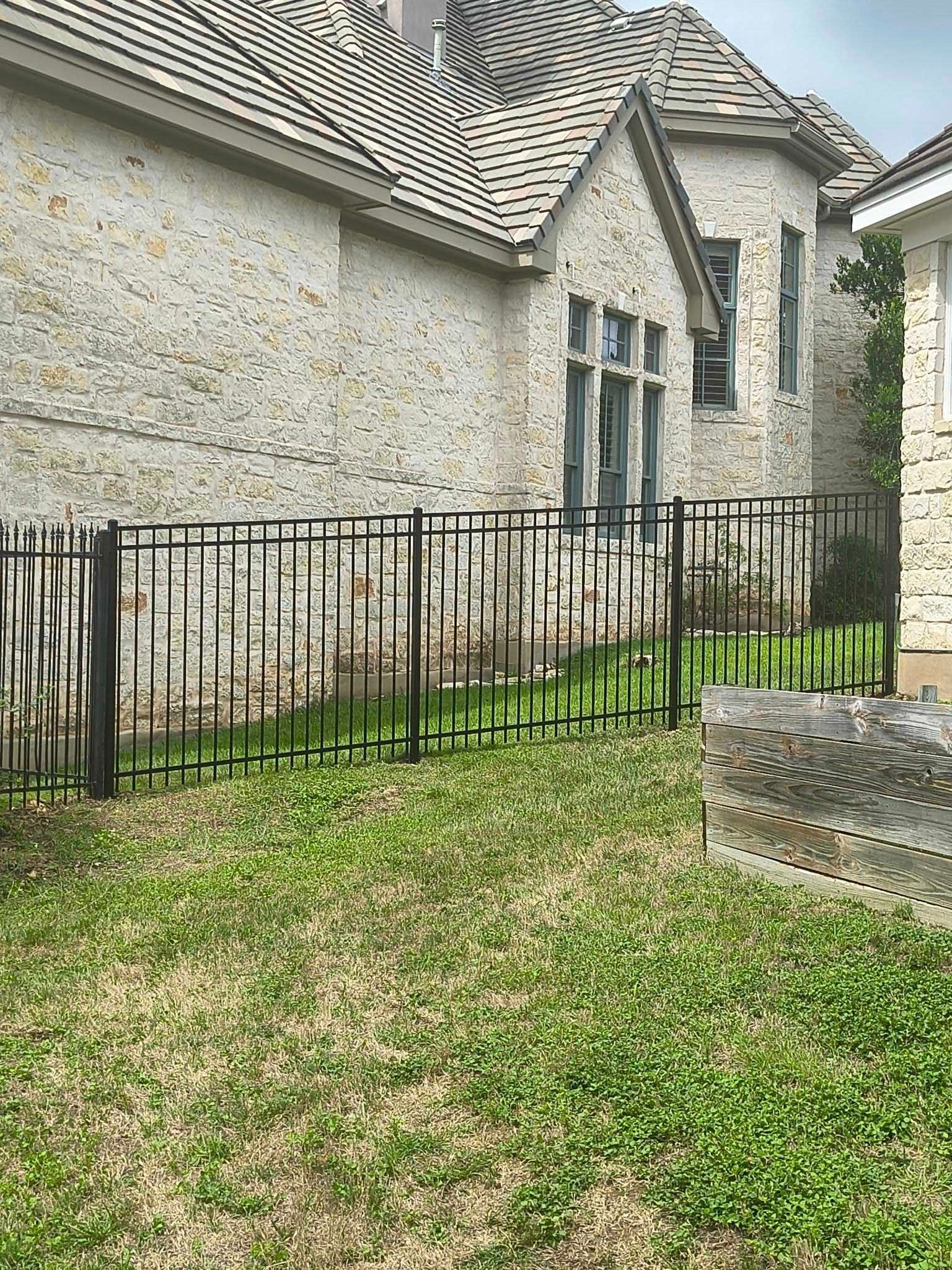 Black metal fence in front of a stone building with a tiled roof and green grass.