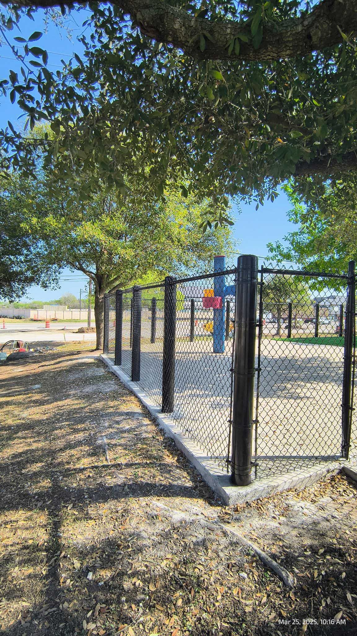 Black fence around a playground with trees.