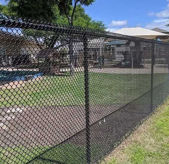 Black chain-link fence bordering a grassy area with a swimming pool visible in the background.