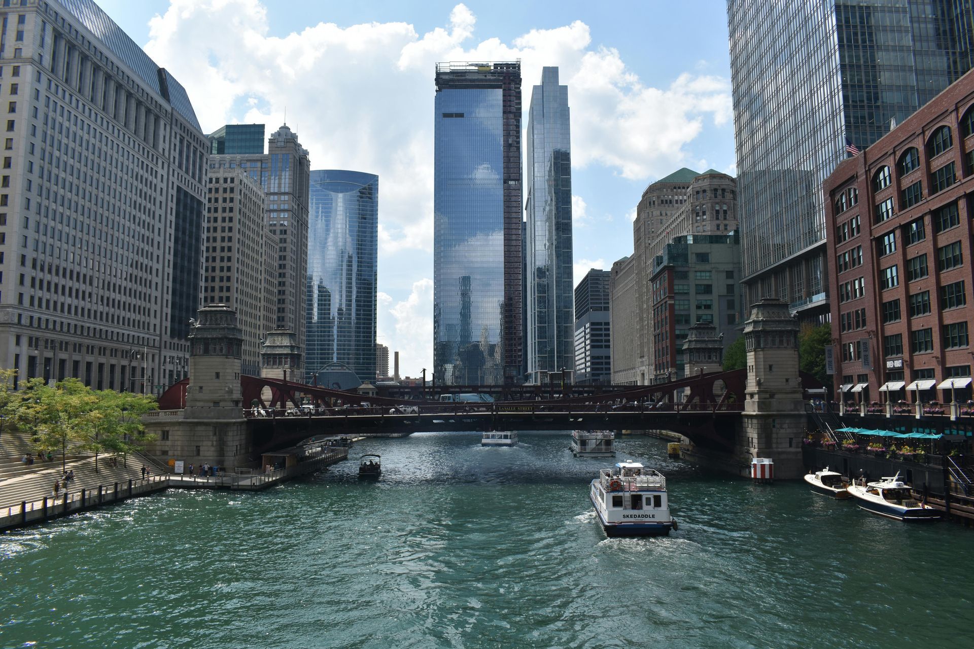 Chicago River with buildings, boats, and a bridge. Blue water and sky.