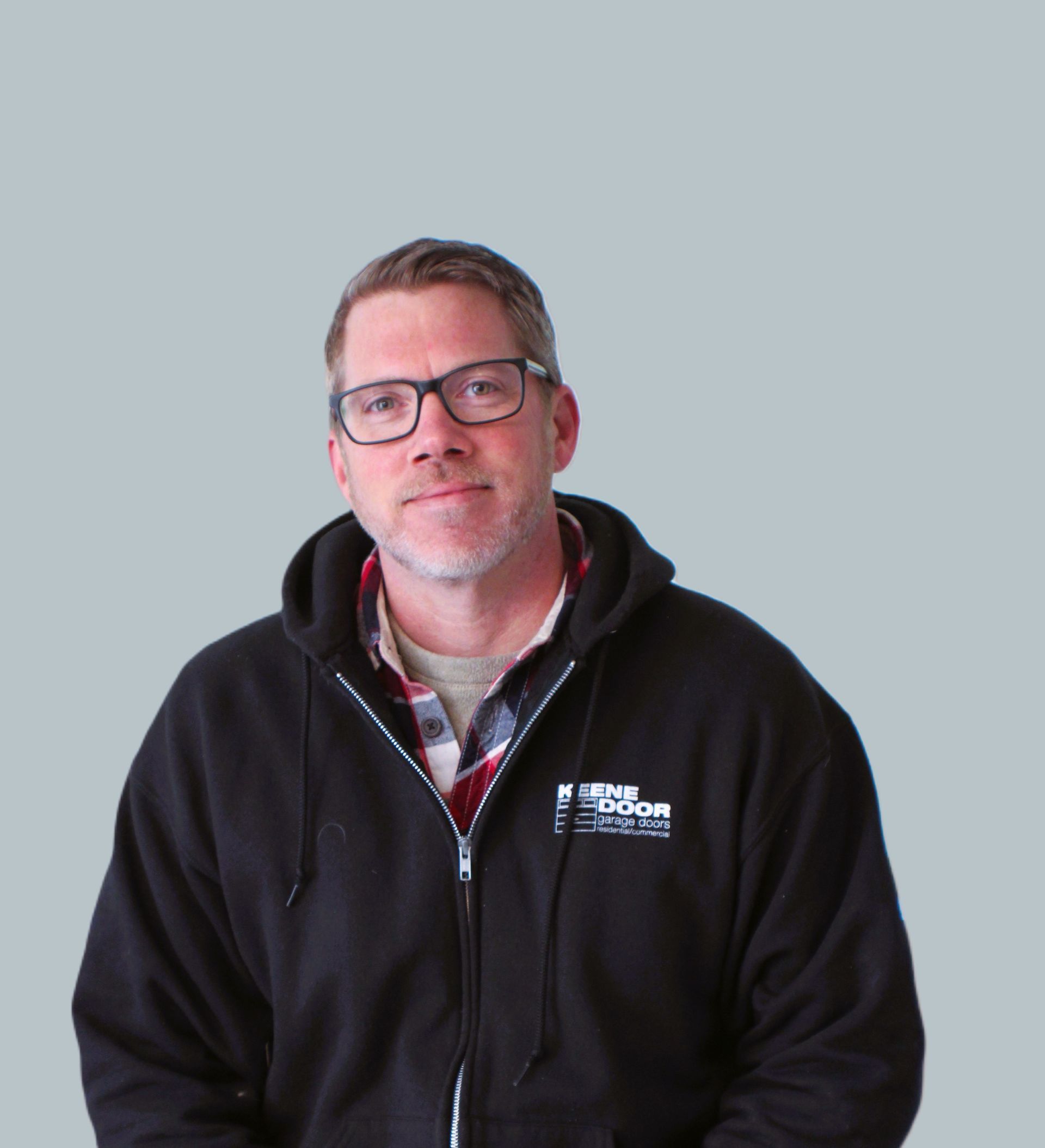 Man wearing glasses and a black hoodie stands against a plain gray background.