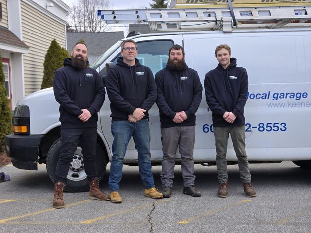 Four workers stand in front of a white local garage van, wearing dark hoodies and boots.