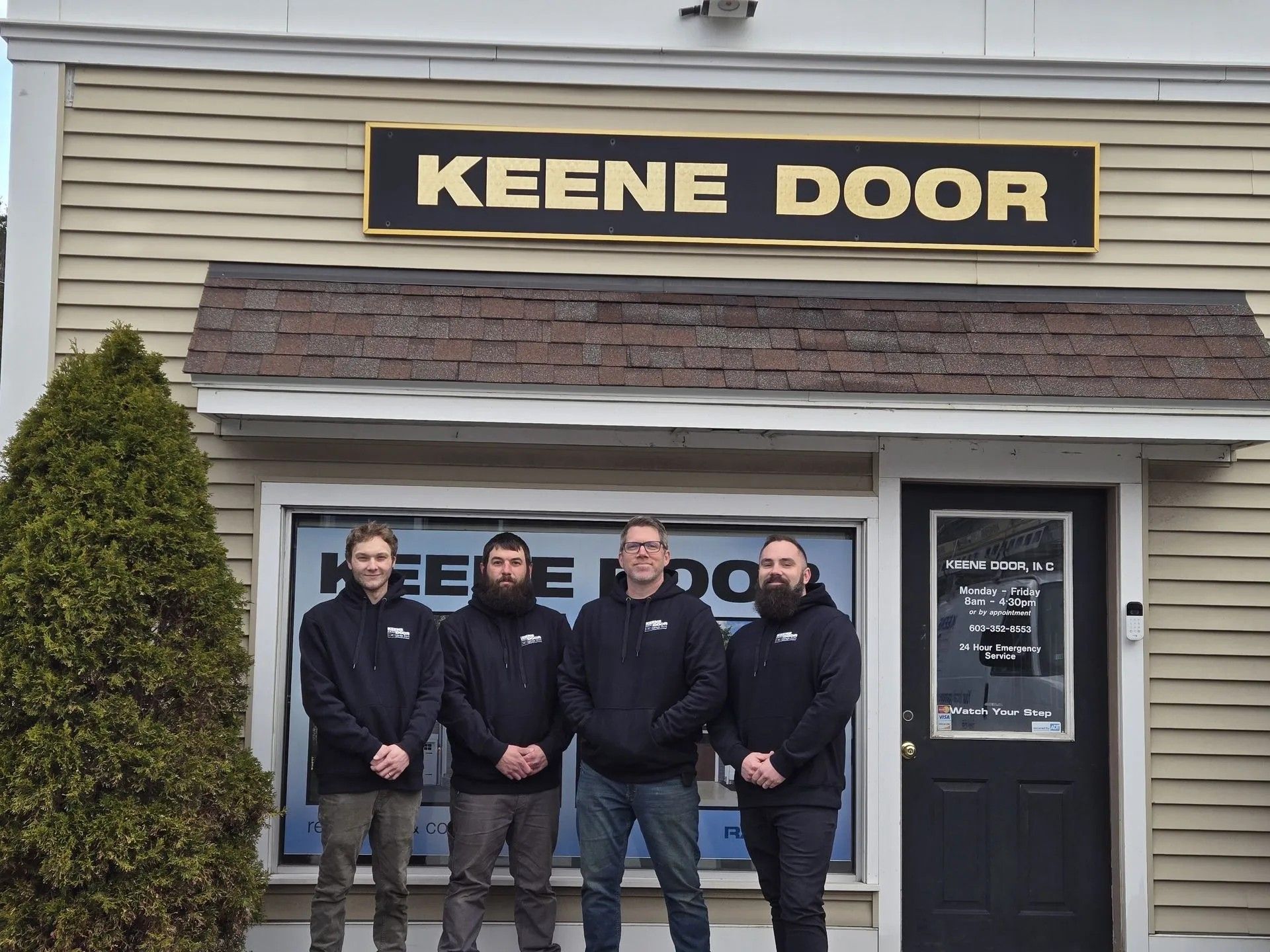 Four men standing outside Keene Door storefront beneath sign, wearing dark jackets