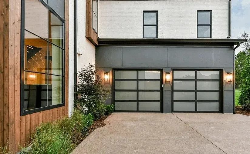 Modern two-story house exterior with gray garage doors and a concrete driveway, seen at dusk