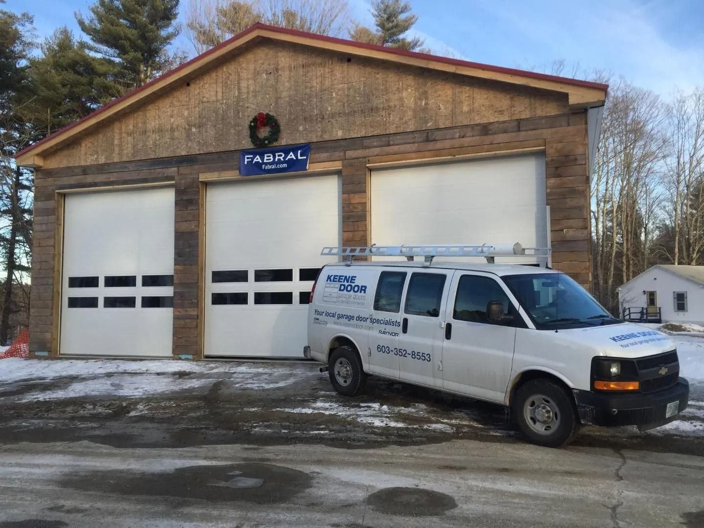 White service van parked in front of a two-bay garage with a FABRAL sign in winter snow.
