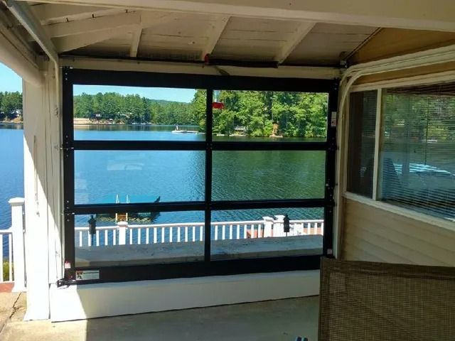 Covered porch overlooking a blue lake with dock and trees, framed by screened windows