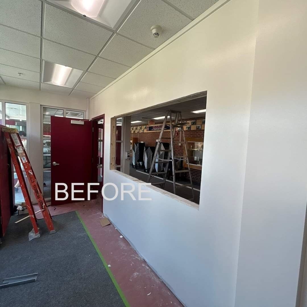 Hallway under renovation with white walls, open doorway, ladder, and construction materials behind a cutout window