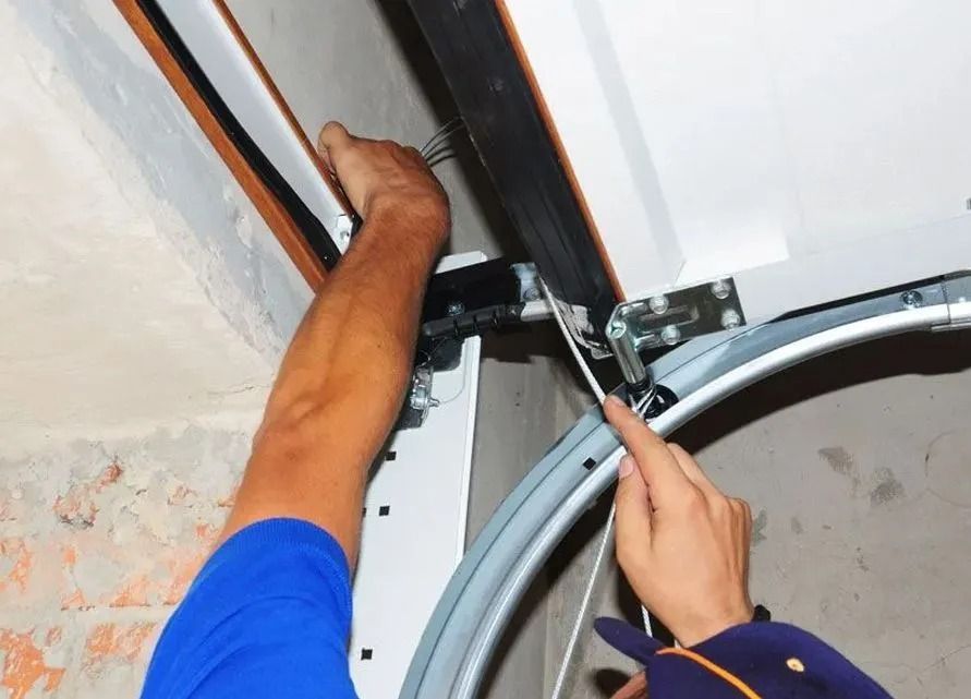 Person adjusting a garage door track with tools near the ceiling