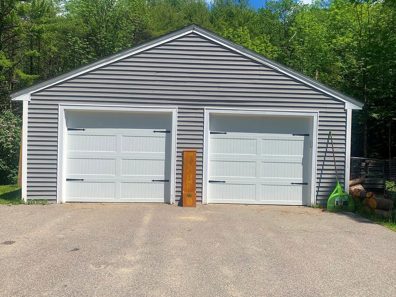 Two-car garage with white doors and gray siding beside a gravel driveway and trees.