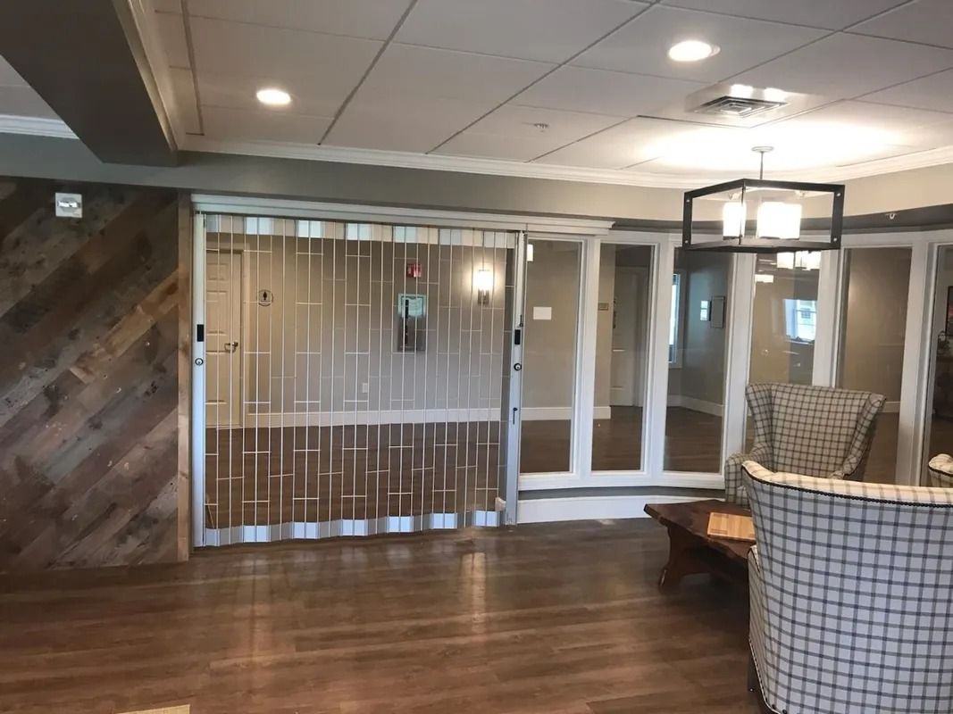 Empty lobby with wood floor, glass storefronts, and wicker chairs under recessed ceiling lights.