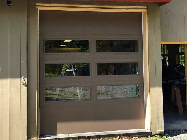Tan garage door with four small windows on a beige building exterior