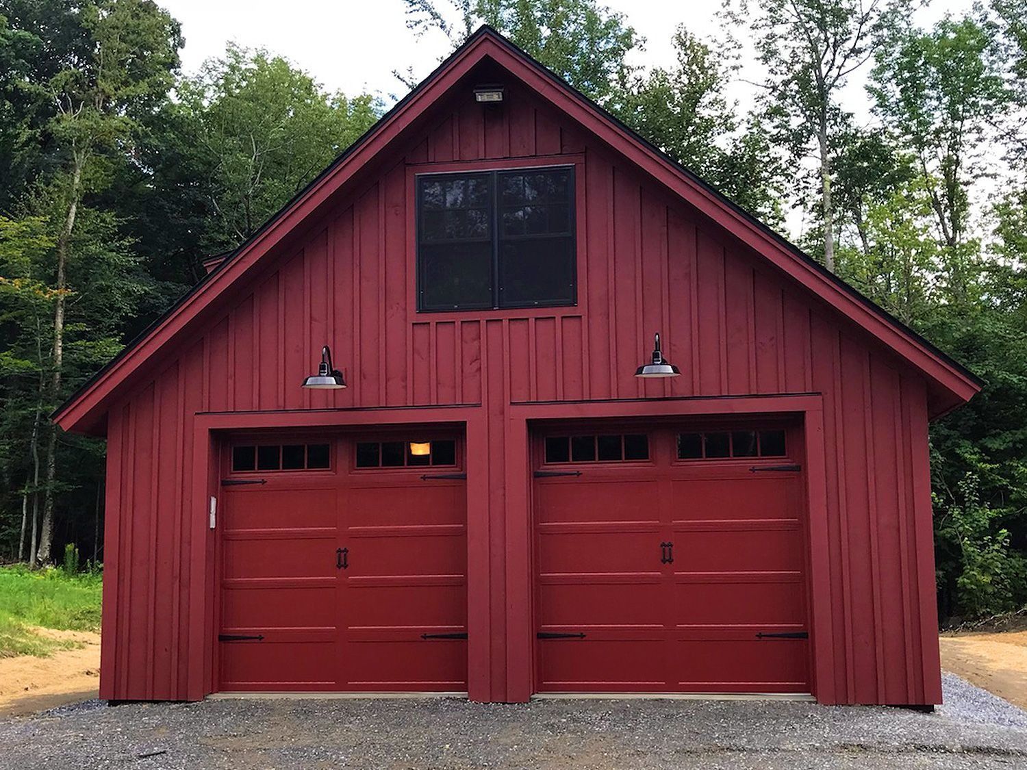 Red barn-style garage with two red doors and a central window, surrounded by trees.