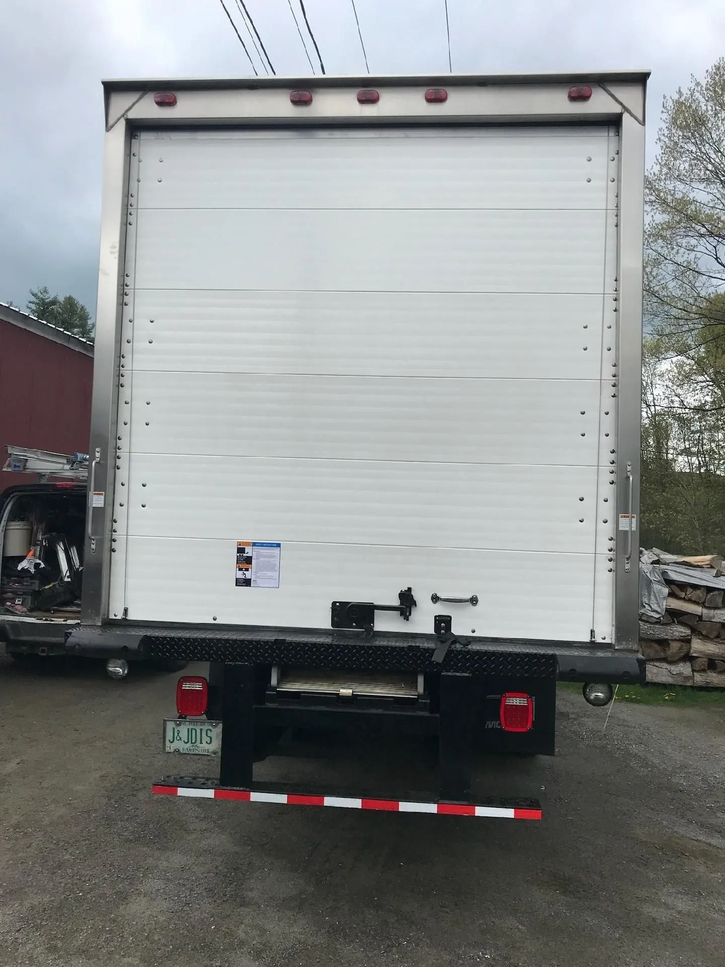 Rear view of a white box truck with a closed roll-up door, parked in a lot.