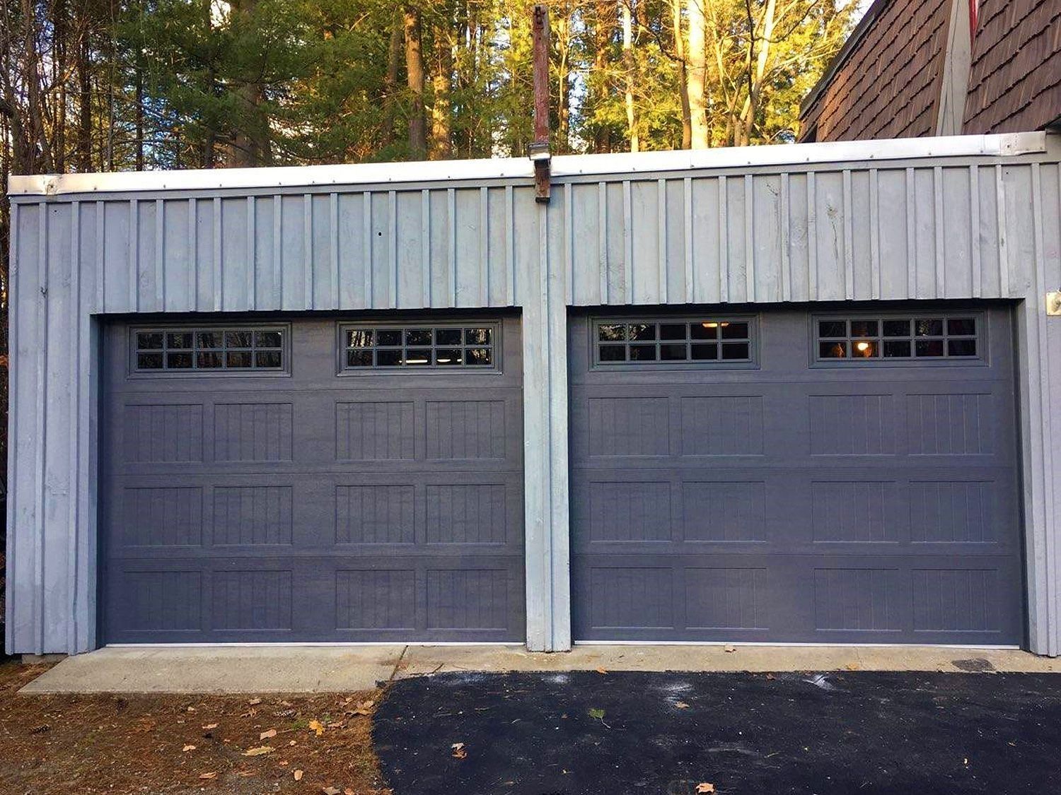 Two gray garage doors on a white-sided detached garage with trees in the background