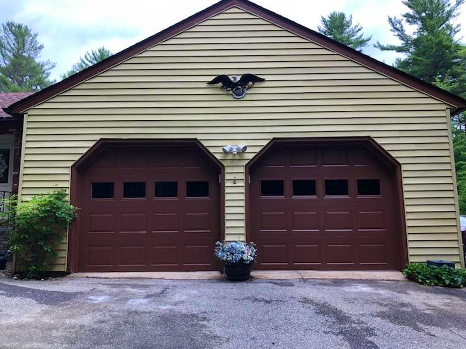 Two brown garage doors on a beige house with a centered planter and black horse emblem above.