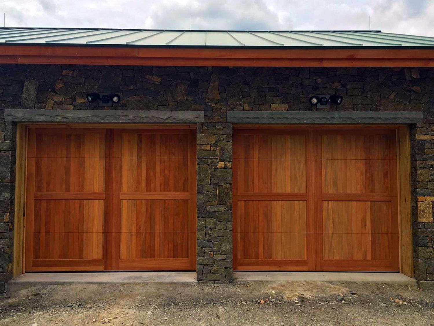 Two wooden garage doors set in a stone facade with a metal roof.
