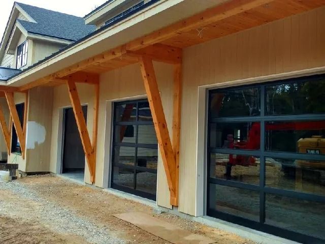 Exterior of a building with wood support posts and large glass garage doors along a gravel walkway