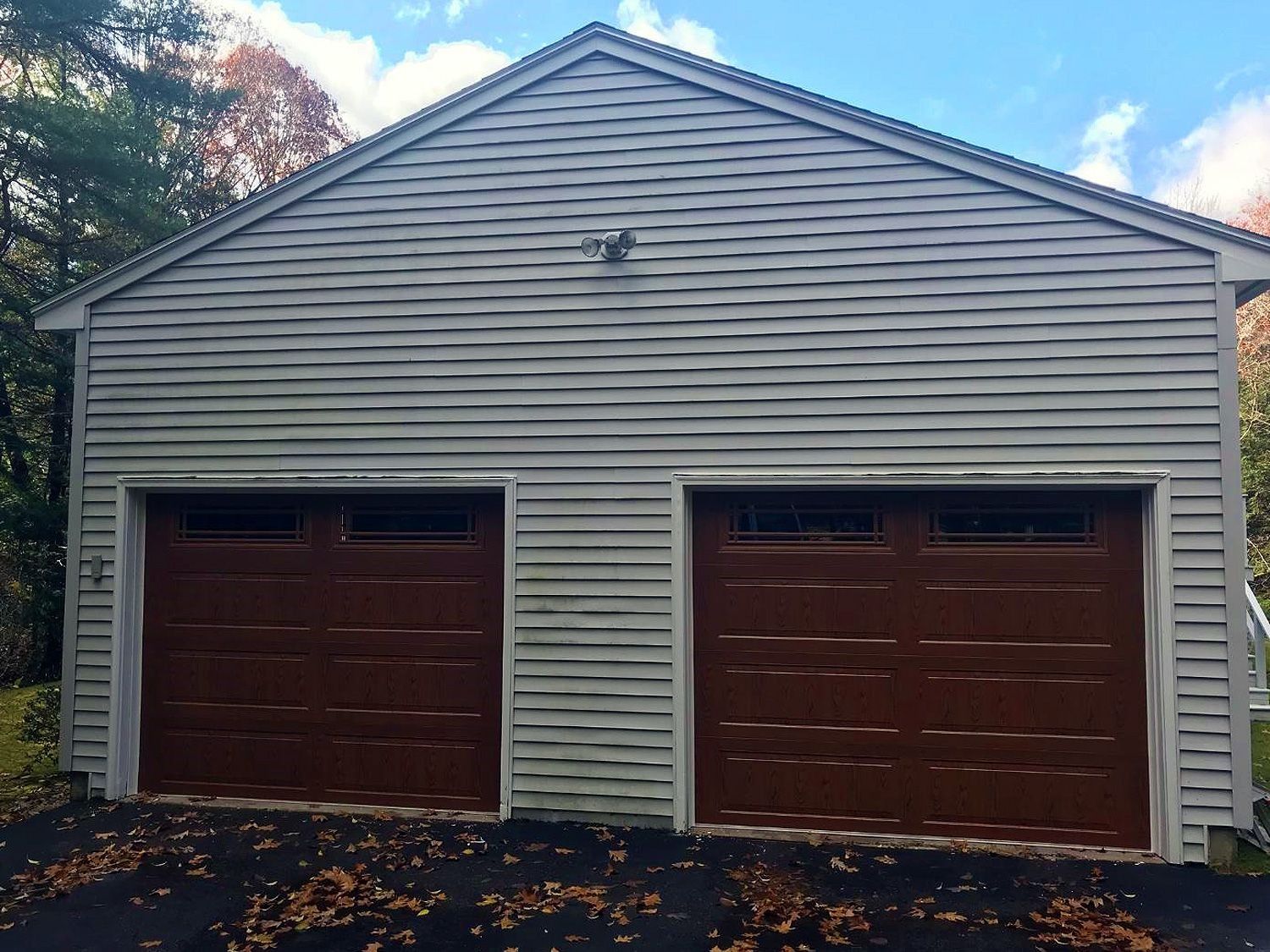 Two-car detached garage with tan siding and brown doors, viewed from the front amid trees