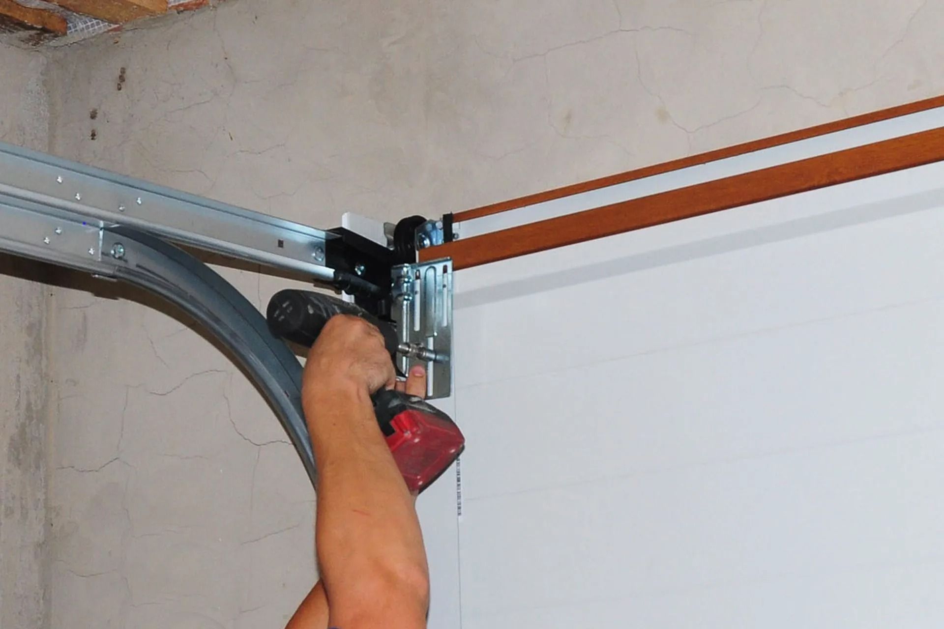 Person using a red drill to work on a garage door track mount