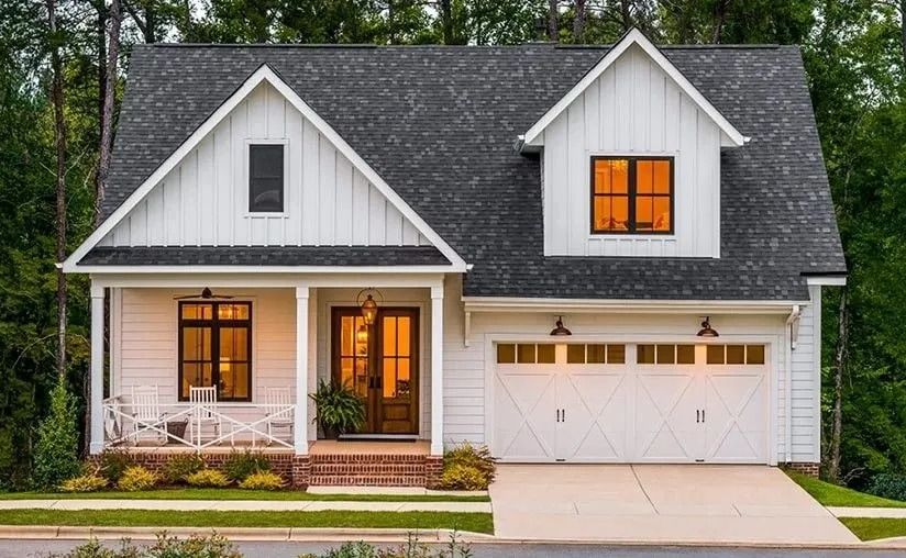White two-story house with a gray roof, lit windows, and a front porch at dusk