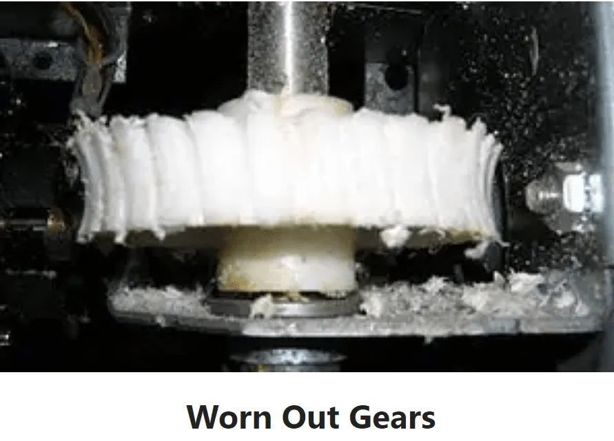 Worn white plastic gears inside a black machine housing, with visible wear and tear