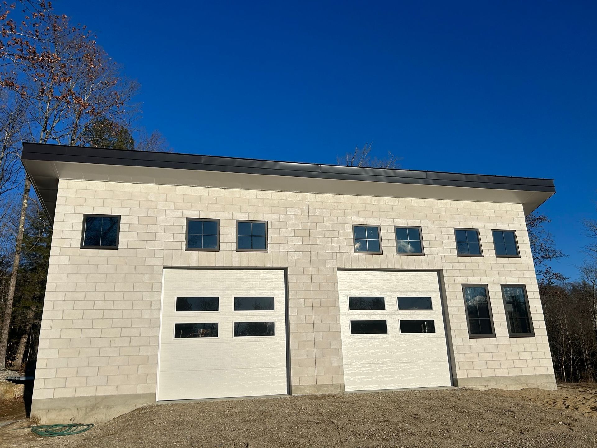 Two-story beige garage building with four white doors under a clear blue sky