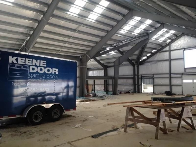 Interior of a large warehouse with a blue KEENE DOOR trailer and work tables on the floor
