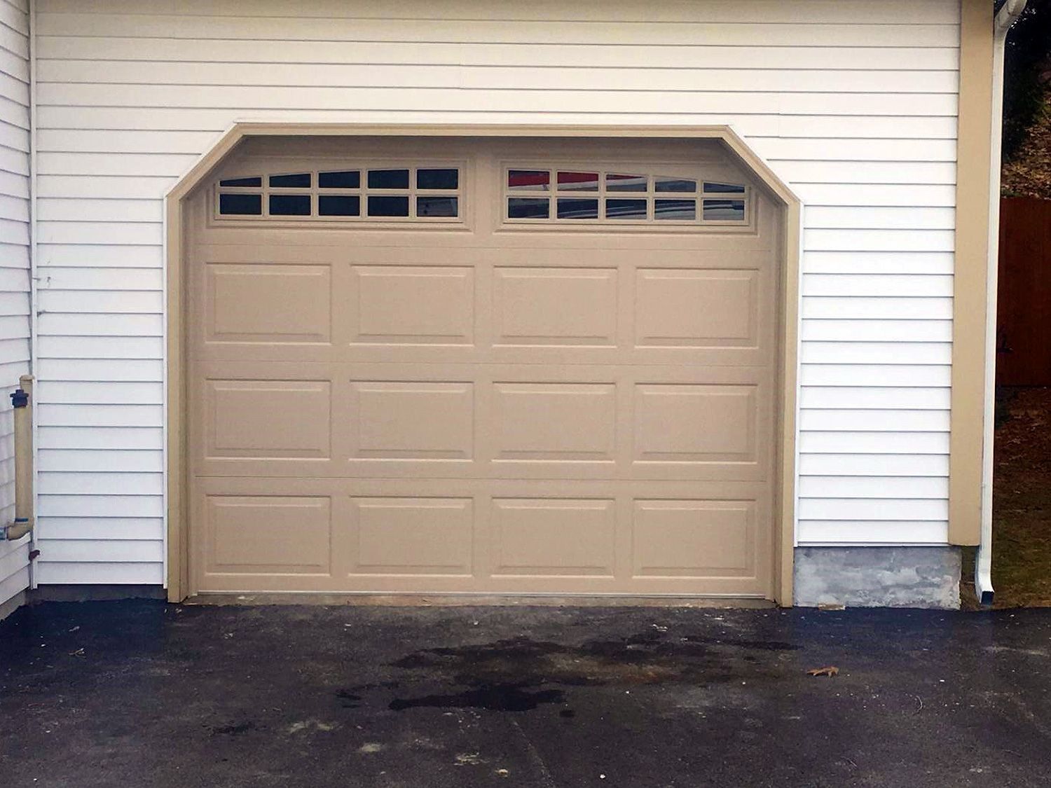 Beige garage door with small window panes on a white-sided house.