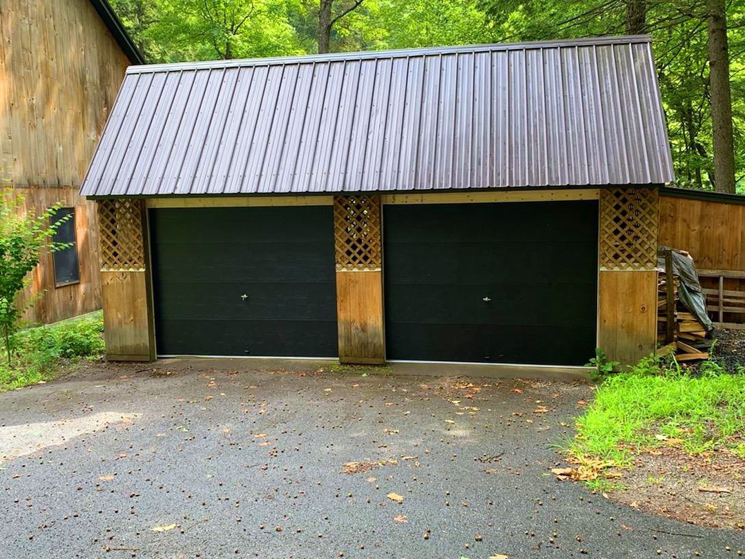 Two-door garage with dark green doors and a metal roof, set in a wooded driveway